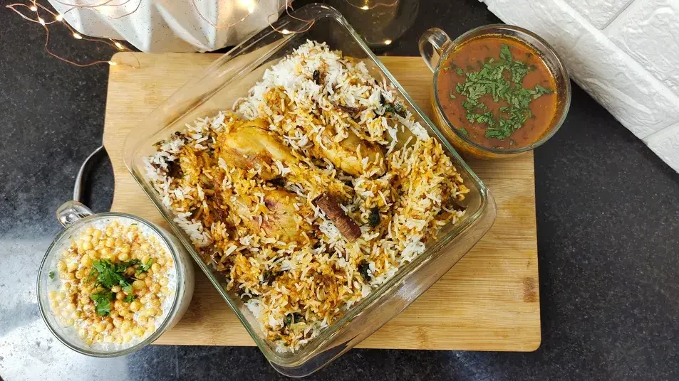 Chicken Biryani with fragrant basmati rice and chicken pieces, served with raita and curry on a wooden board - Cityscape Mumbai Tours food guide
