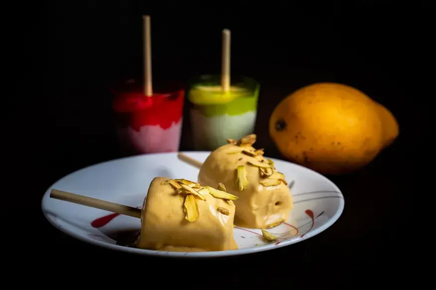 Mango Kulfi sticks topped with pistachios, served on a plate with a fresh mango - Cityscape Mumbai Tours food guide
