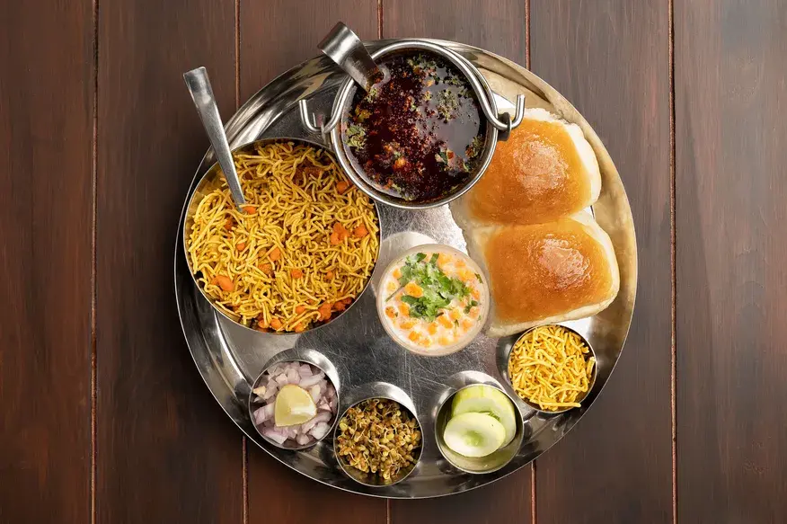 Spicy Misal Pav thali with sprouted lentil curry, farsan, pav, onions and lime served in a steel platter - Cityscape Mumbai Tours food guide