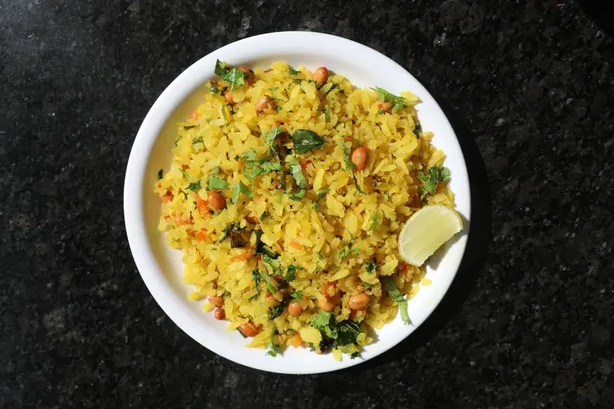 Maharashtrian Poha (flattened rice) garnished with peanuts, coriander and curry leaves, served with a lime wedge - Cityscape Mumbai Tours food guide