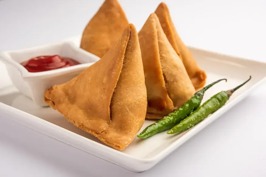 Crispy fried Samosas served with tomato ketchup and green chillies on a white tray - Cityscape Mumbai Tours food guide