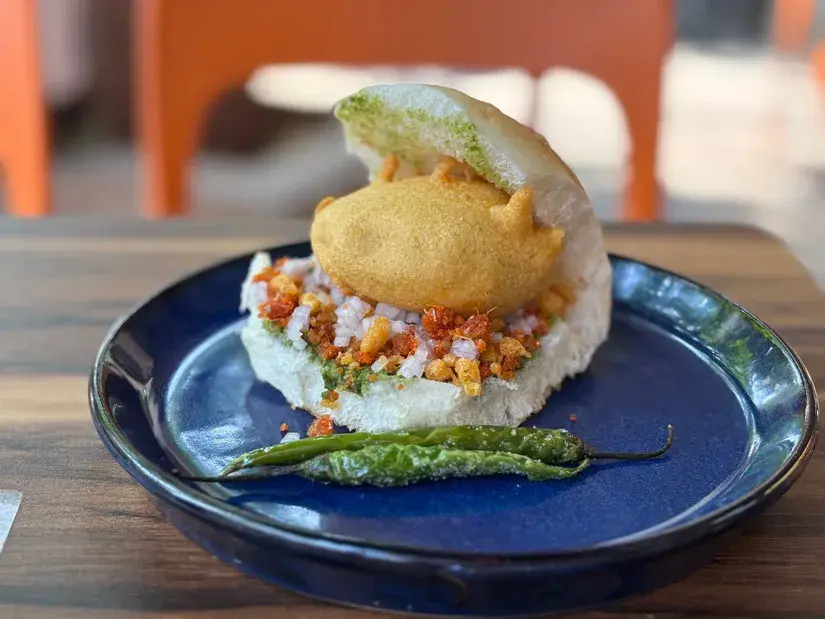 Mumbai's iconic Vada Pav with crispy potato fritter, garlic chutney and fried green chilli, served on a blue plate - Cityscape Mumbai Tours food guide