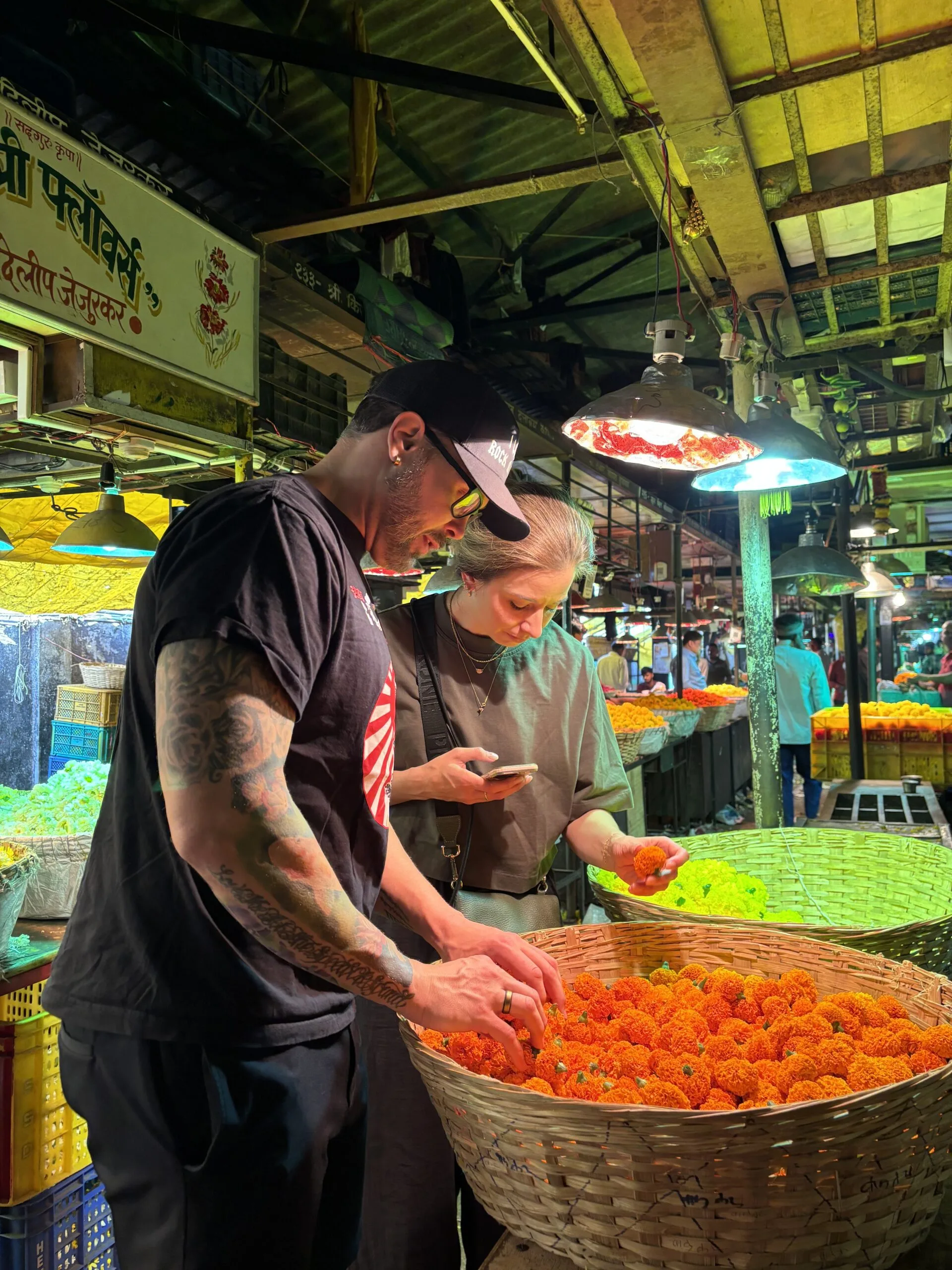 Travellers browsing baskets of fresh marigold flowers at a traditional Mumbai flower market , Cityscape Mumbai Tours.