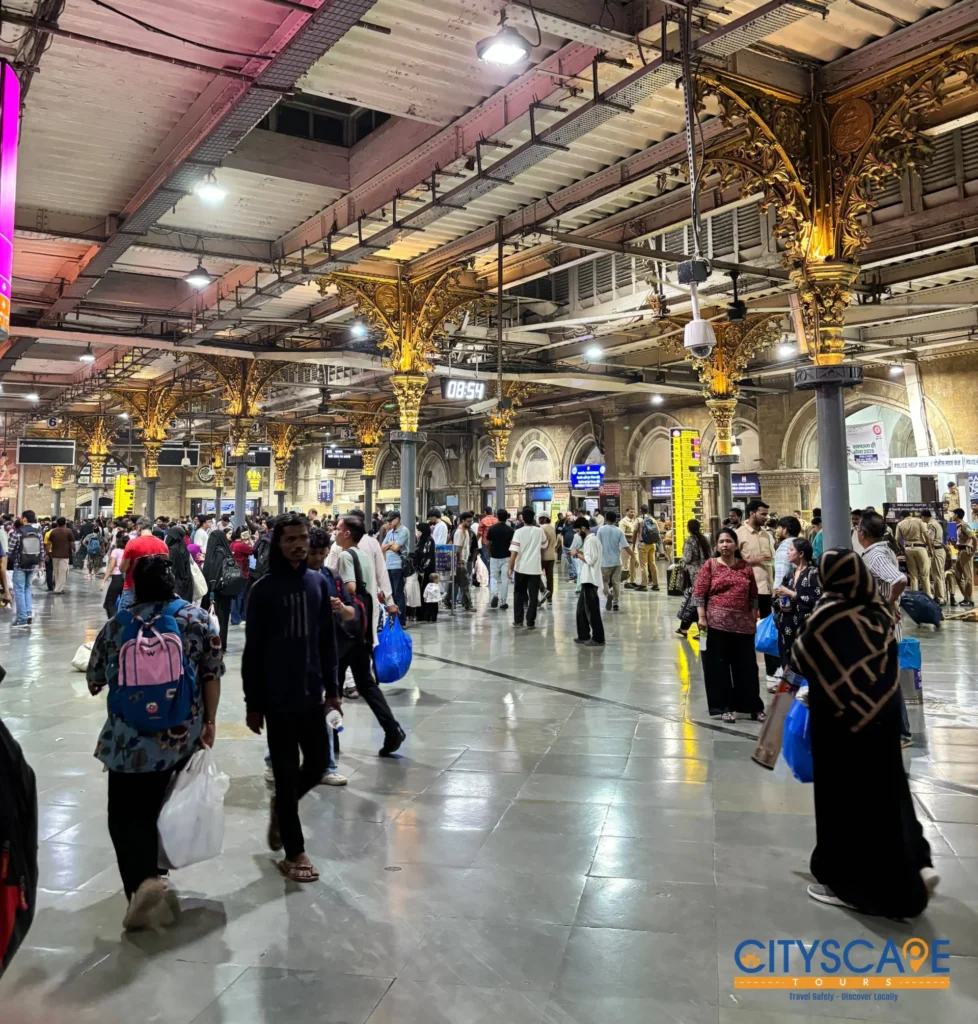 Commuters walking across the busy concourse of Churchgate Railway Station under ornate golden pillars, on the Mumbai dawn tour by Cityscape Mumbai Tours.