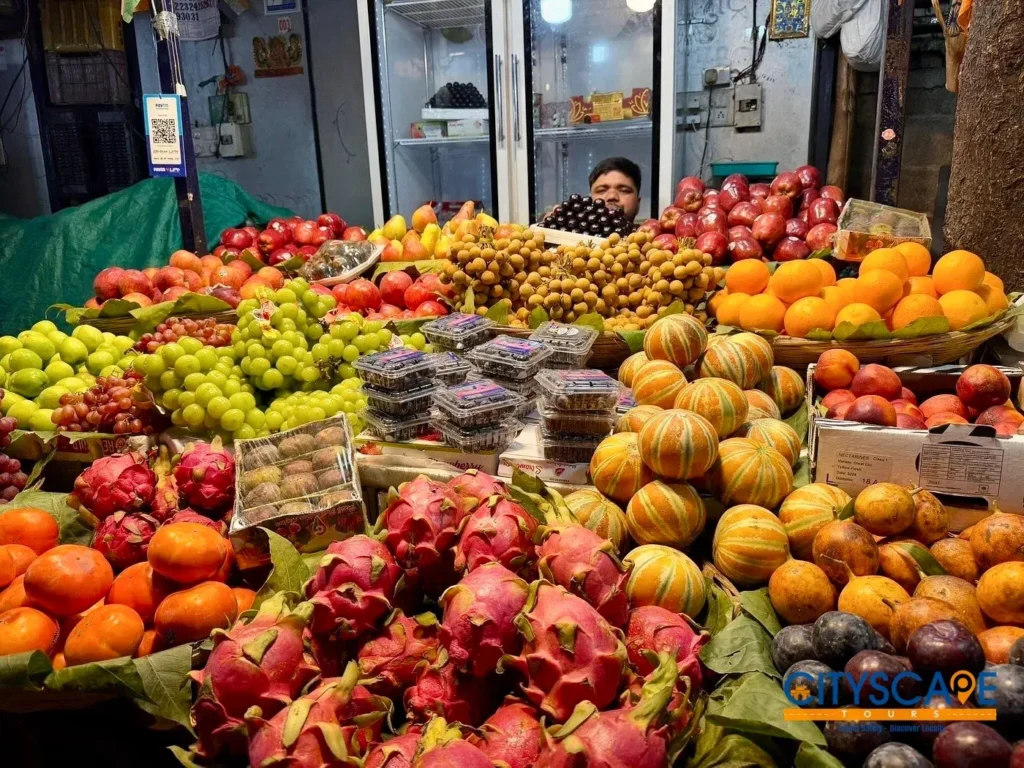 Fruit stall piled high with dragon fruit, green grapes, oranges, apples and melons at Dadar Fruit and Vegetable Market, on the Mumbai dawn tour by Cityscape Mumbai Tours.
