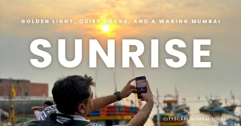 Visitor taking a phone photo of the golden morning sun over the harbour and fishing boats, on the Mumbai dawn tour by Cityscape Mumbai Tours.
