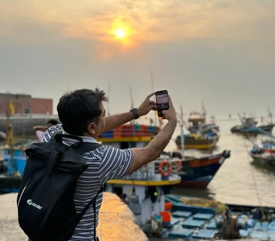 Visitor taking a phone photo of the golden morning sun over the harbour and fishing boats, on the Mumbai dawn tour by Cityscape Mumbai Tours.